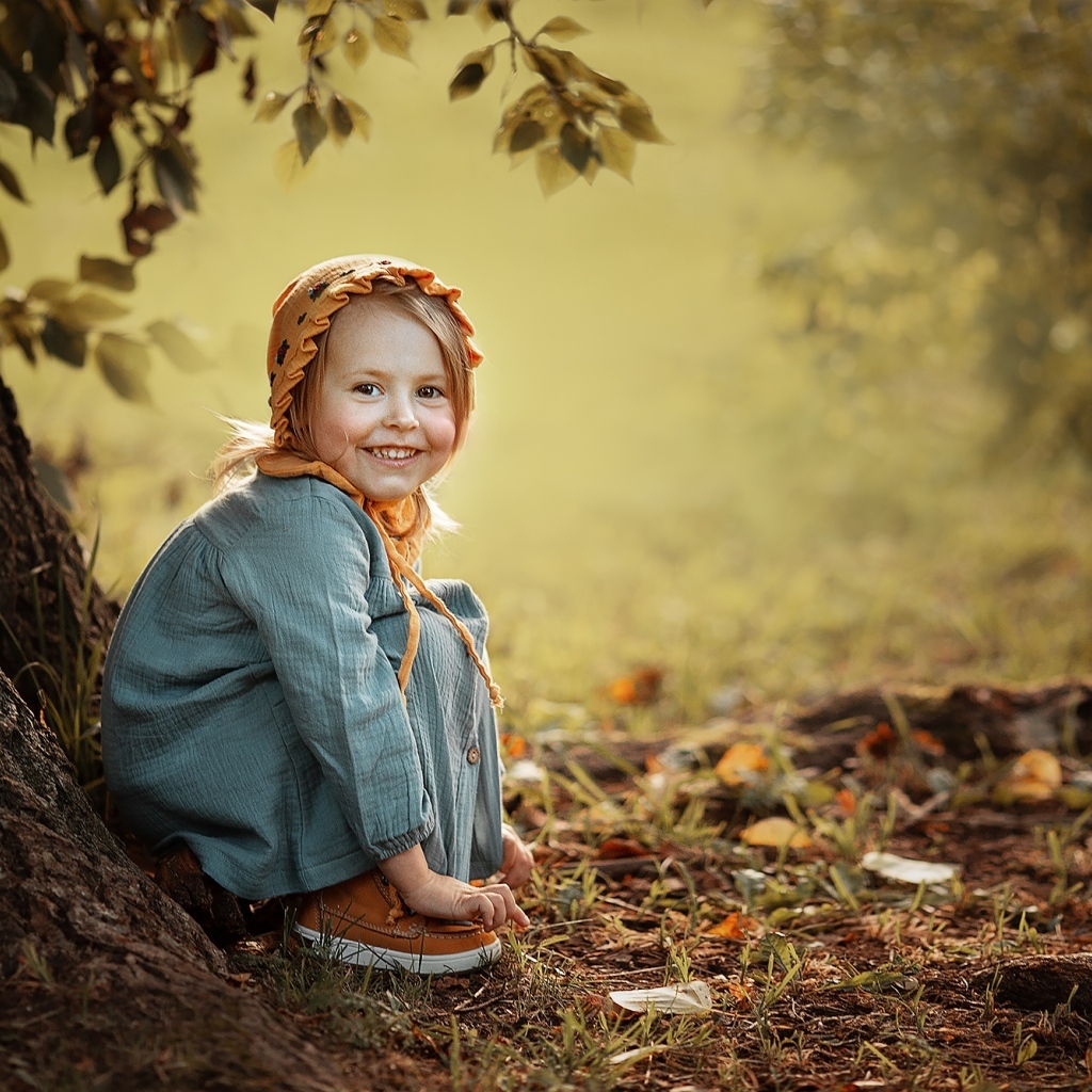 Красивая улыбающаяся девочка сидит под деревом
