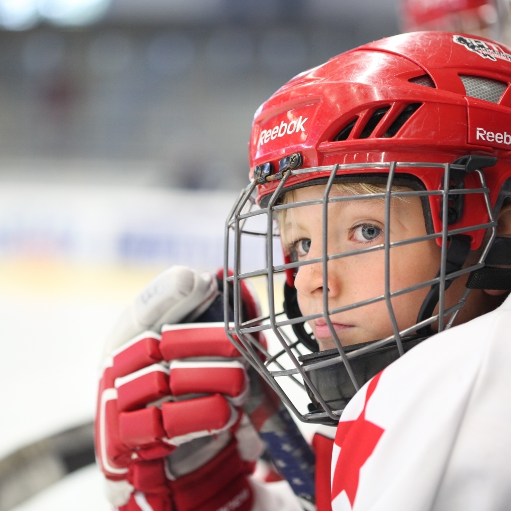 Мальчик в красном шлеме хоккеиста на поле
