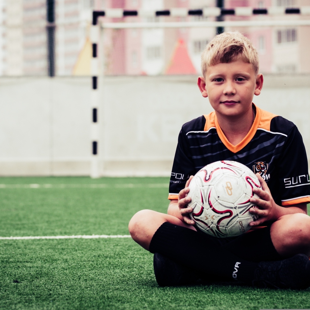 Мальчик футболист сидит на траве с мячом