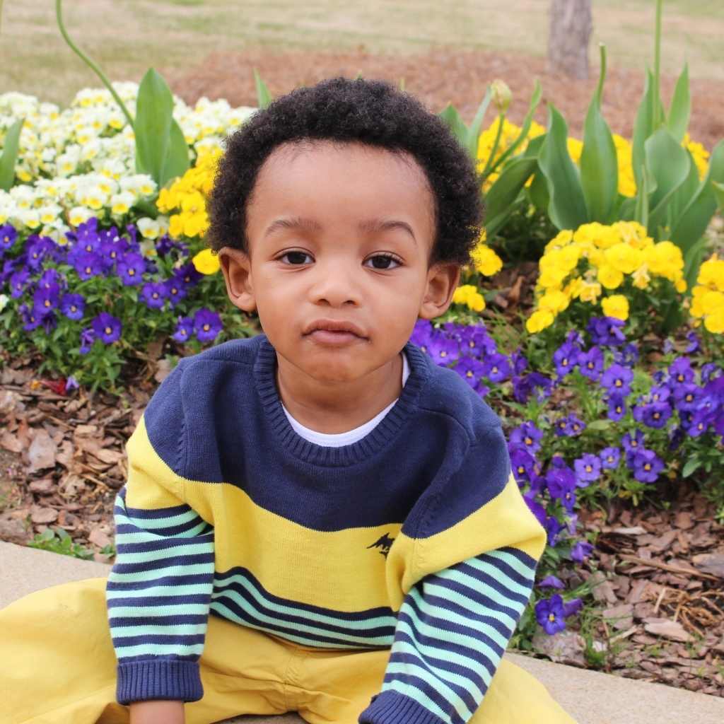 Темнокожий мальчик у клумбы с цветами 