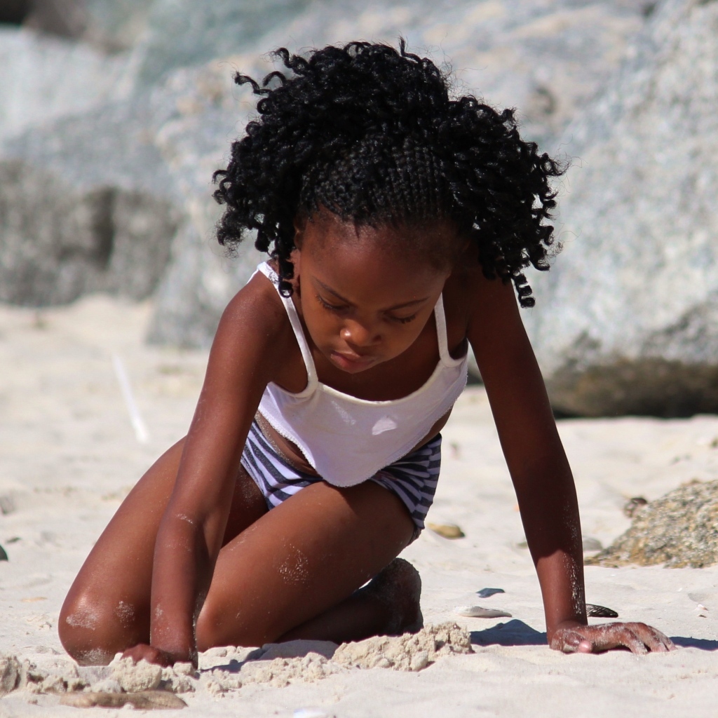 Темнокожая маленькая девочка играет на песке на пляже