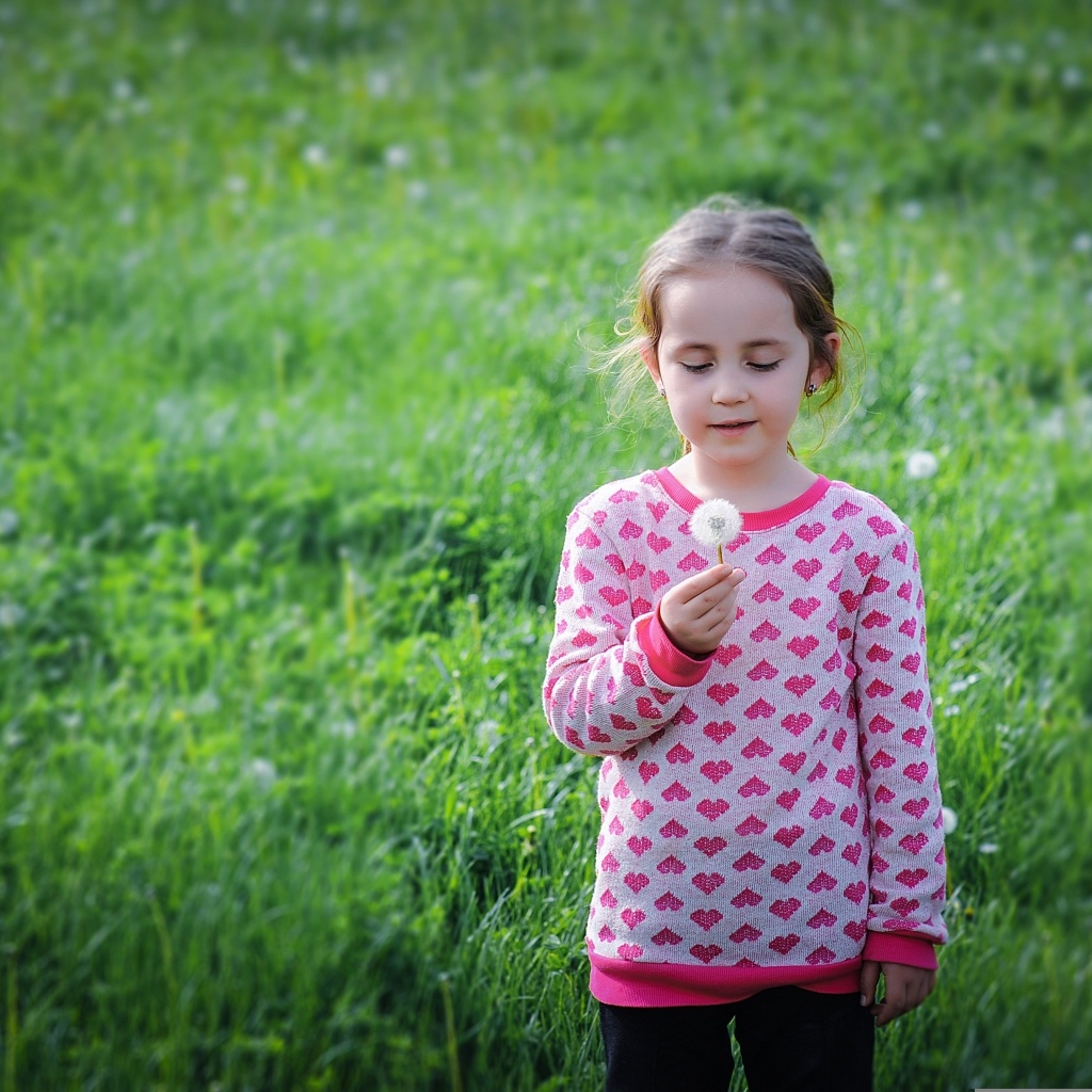 Девочка с одуванчиком на поле с зеленой травой