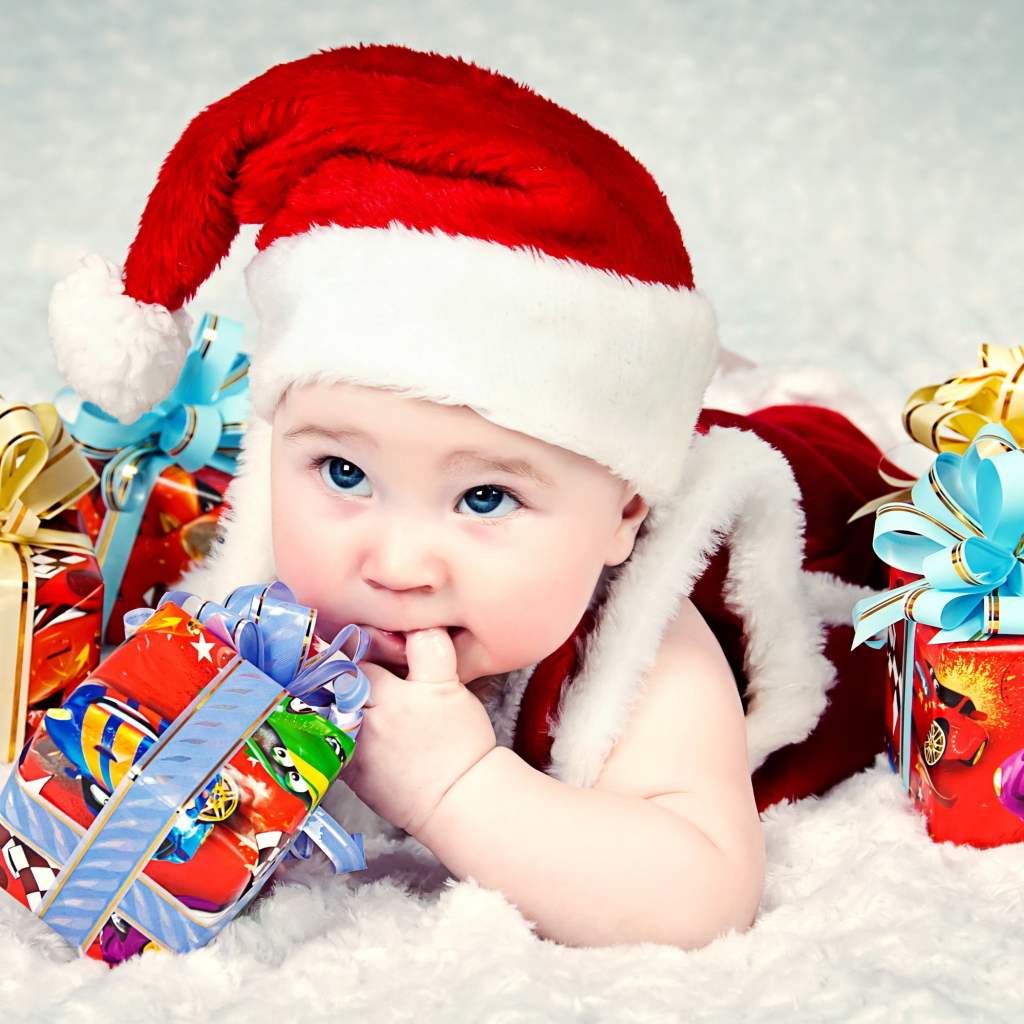 Грудной ребенок в новогодней шапке с подарками на покрывале