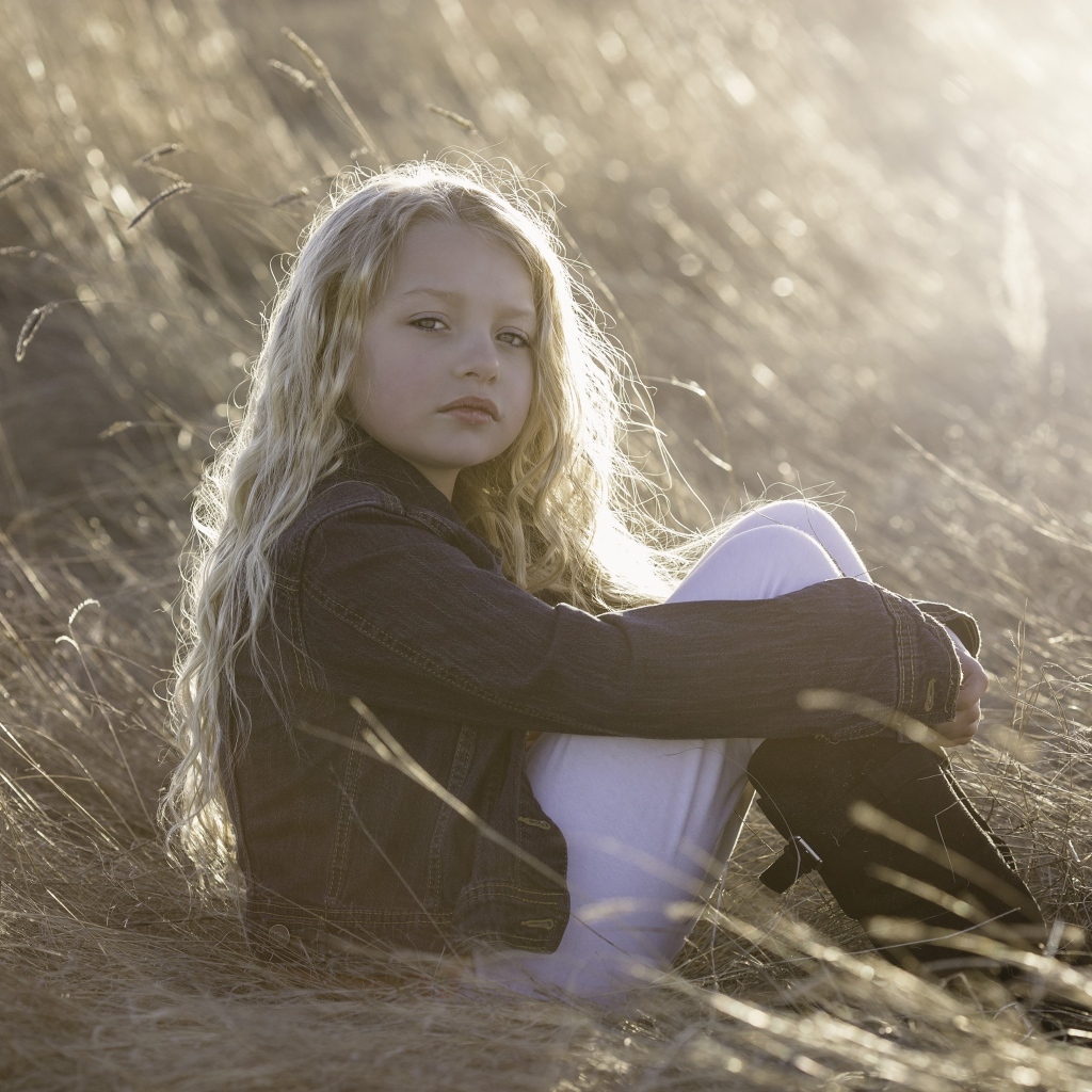 Маленькая светловолосая девочка сидит на сене