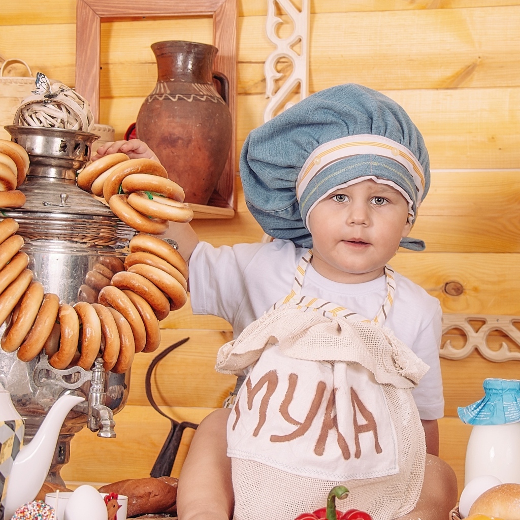 Маленький мальчик повар с продуктами и самоваром на столе