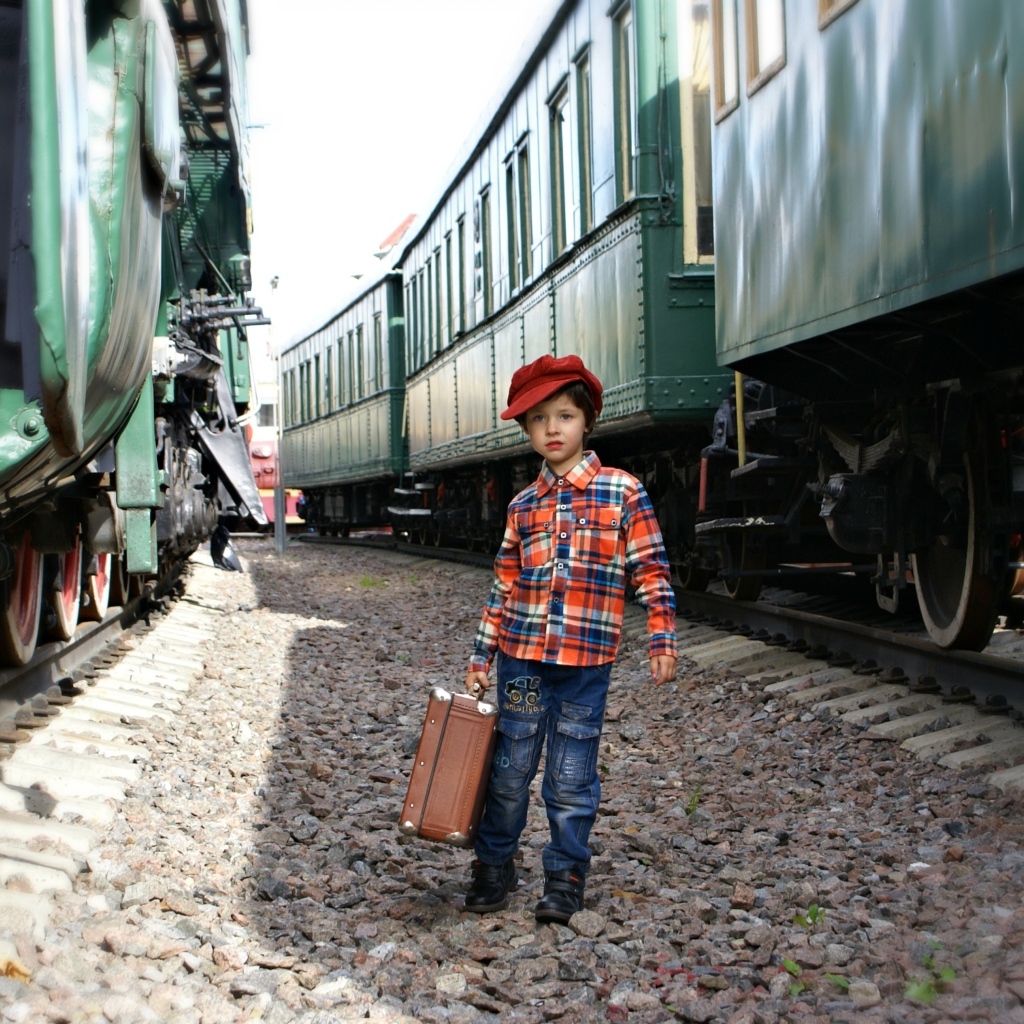 Маленький мальчик с чемоданом у вагонов