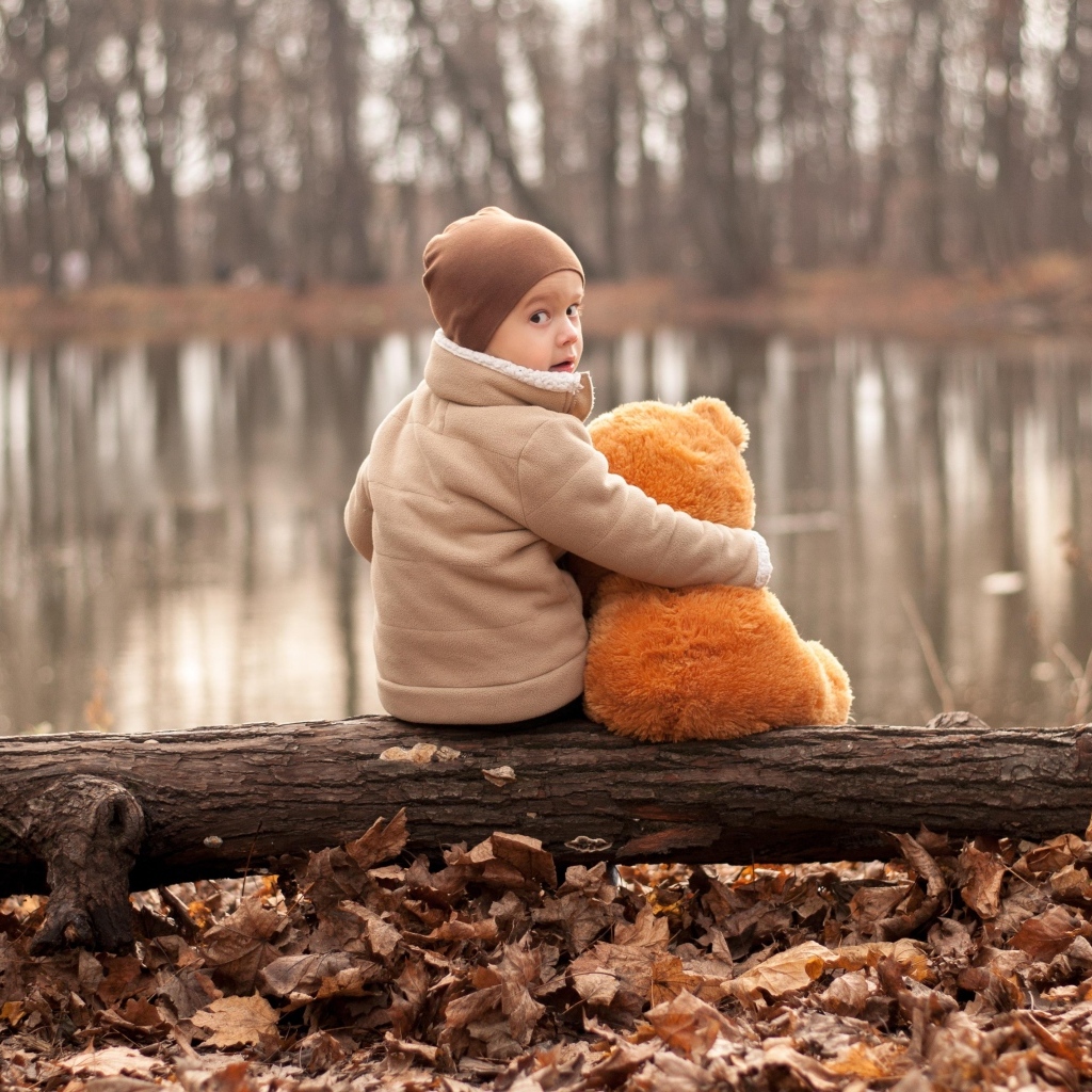 Маленький мальчик с игрушкой сидят на колоде у озера осенью