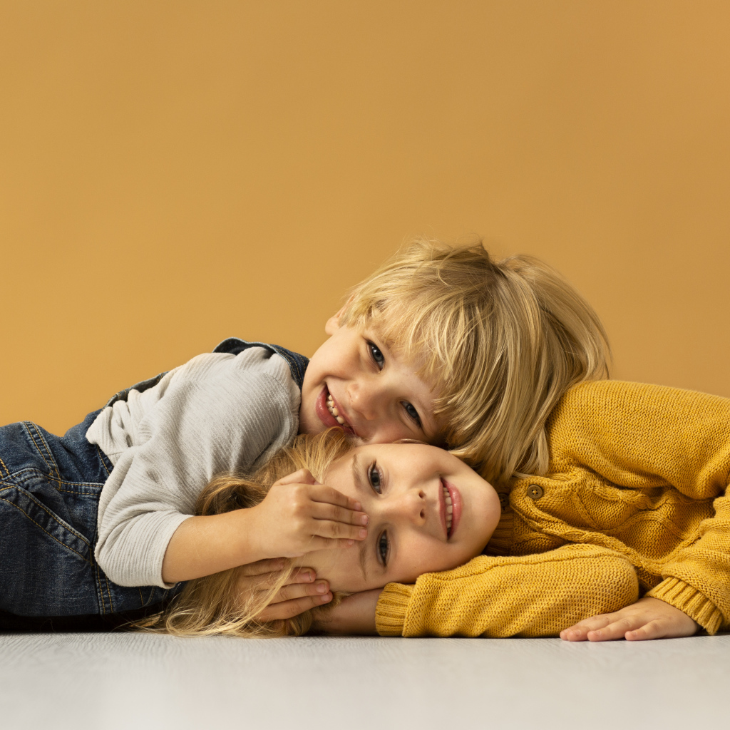 Маленькие брат и сестра лежат на полу на желтом фоне