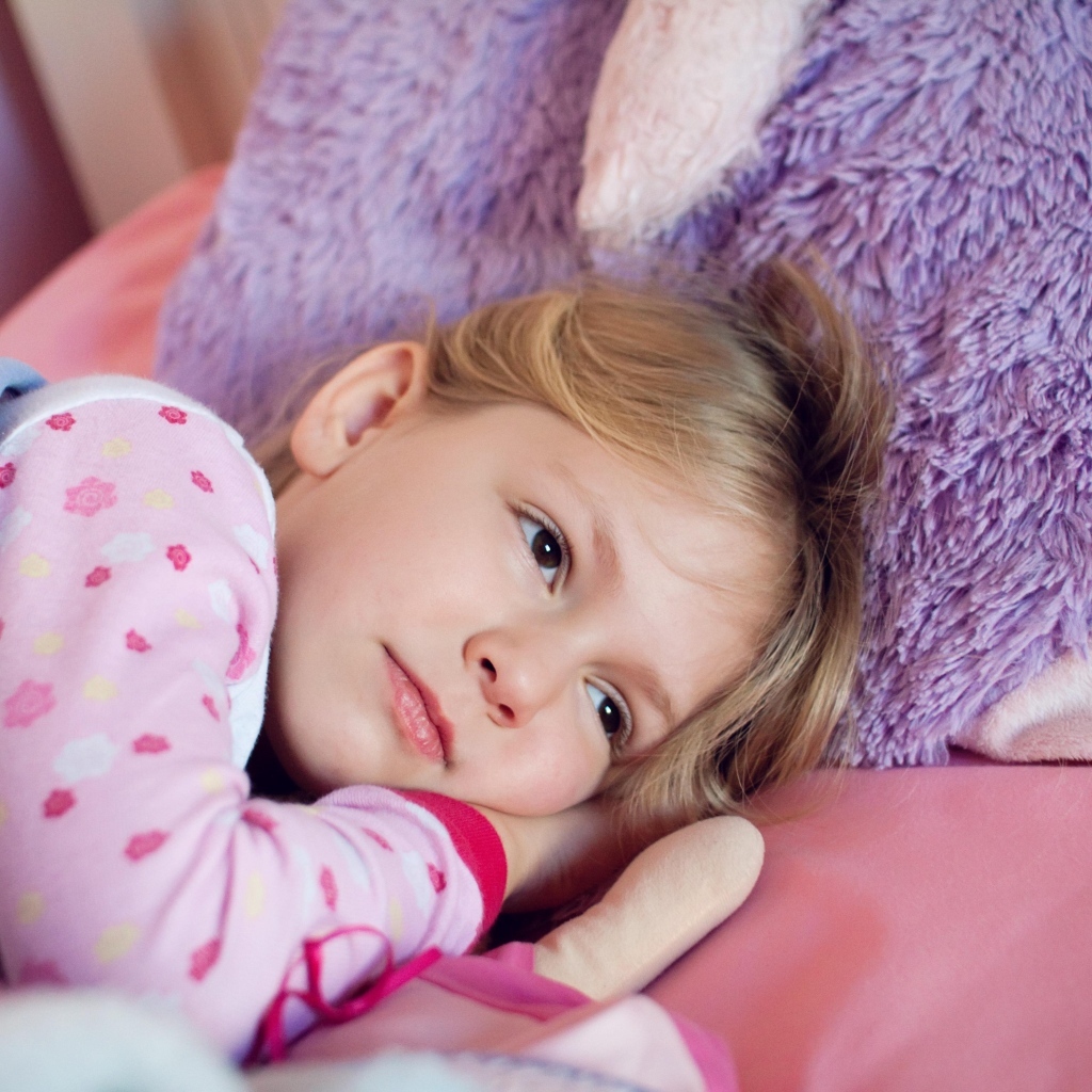 Маленькая кареглазая девочка лежит в кровати 