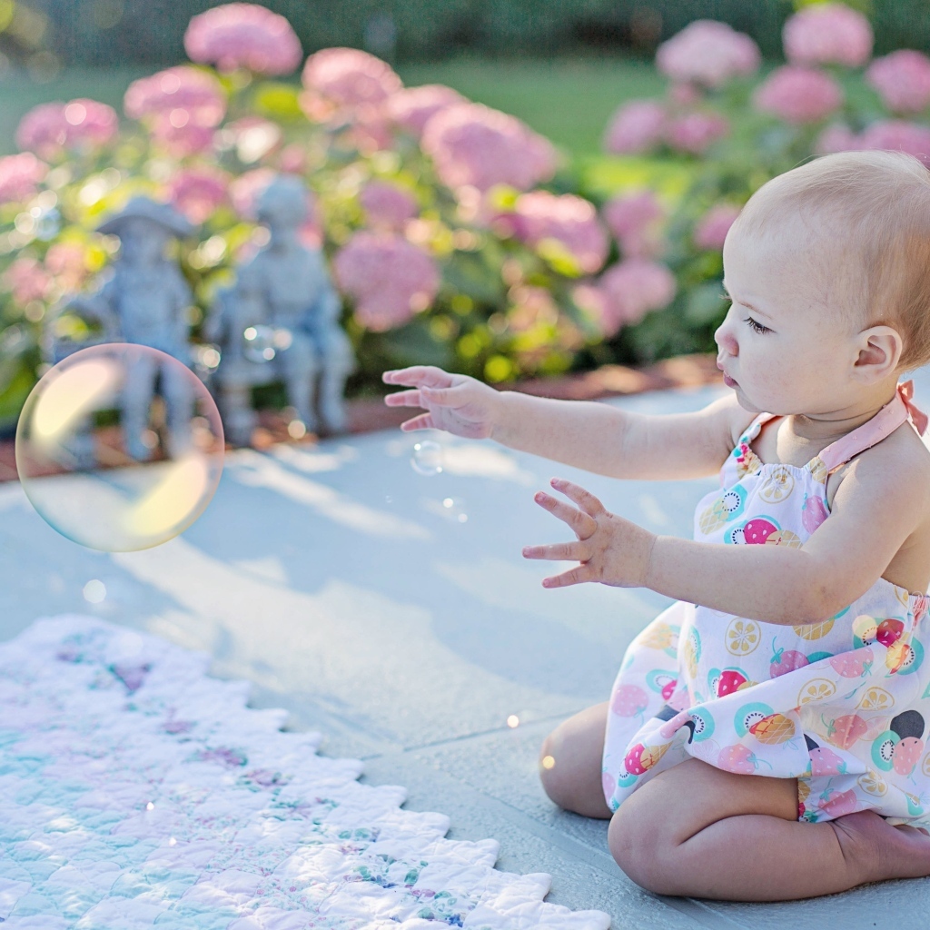 Маленькая девочка ловит мыльный пузырь на улице летом