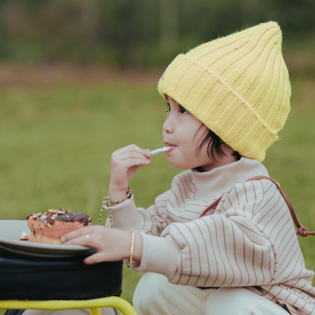 Маленькая девочка в желтой шапке ест пирожное