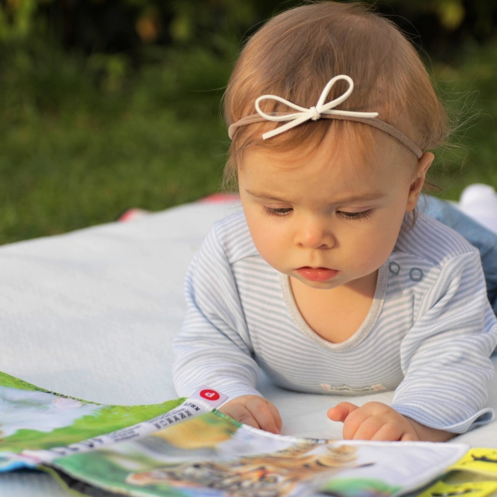 Маленькая девочка с книгой на белом покрывале