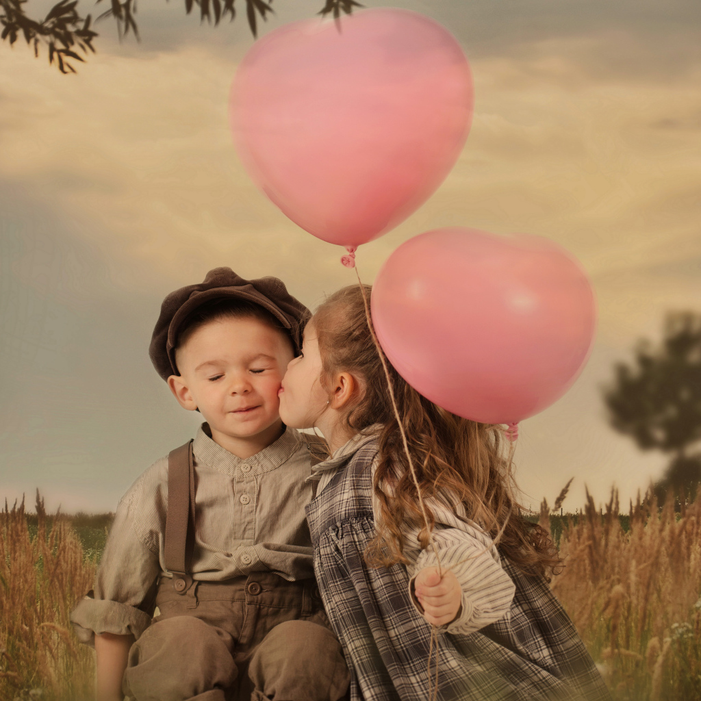 Маленькая девочка с шариками целует мальчика