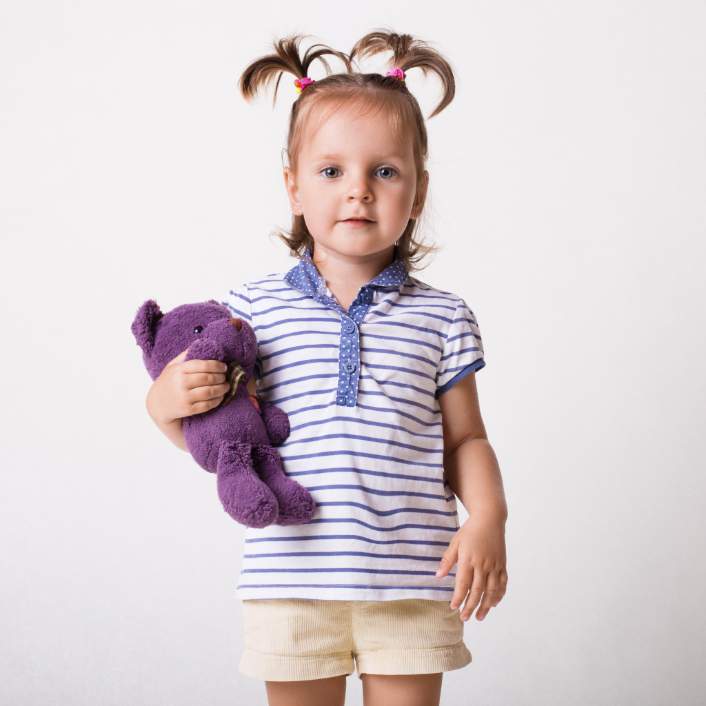 Маленькая девочка с игрушечным медведем на сером фоне