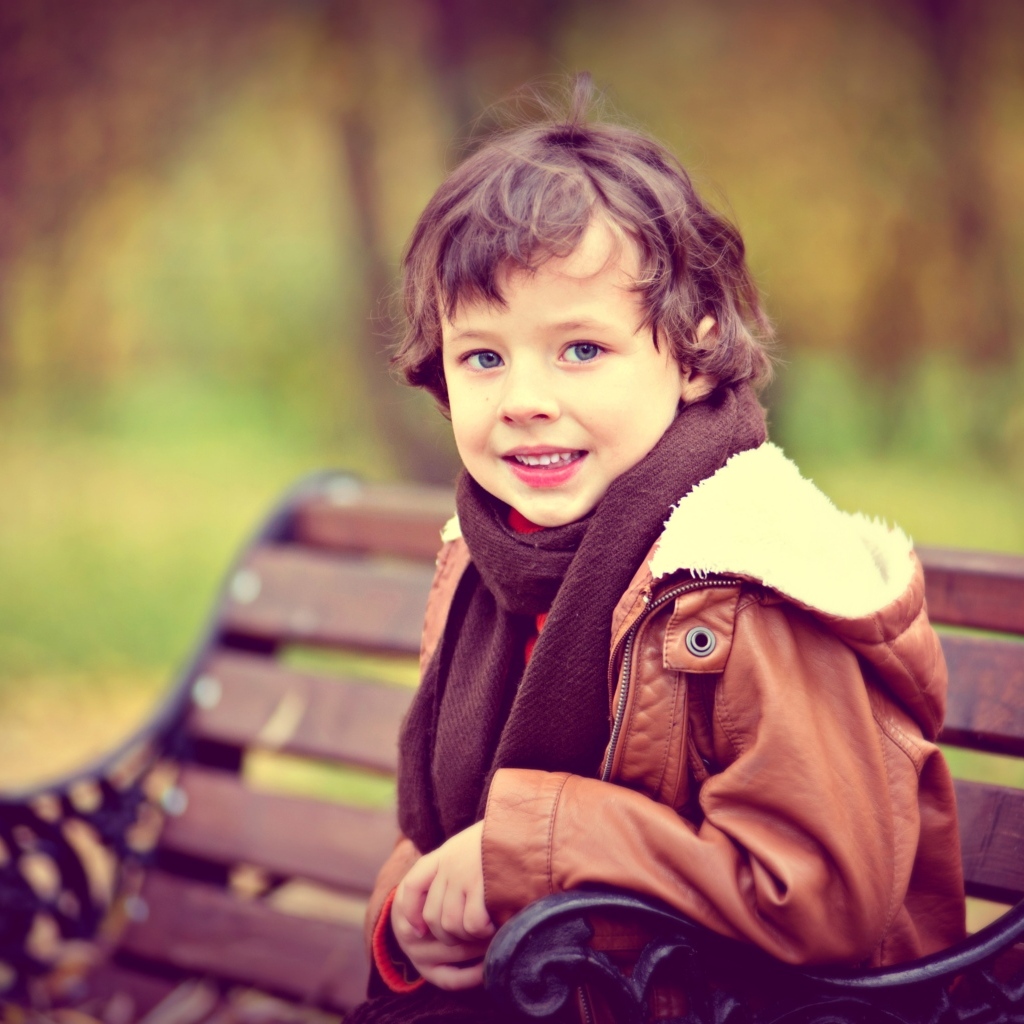 Маленький улыбающийся мальчик на лавке в парке