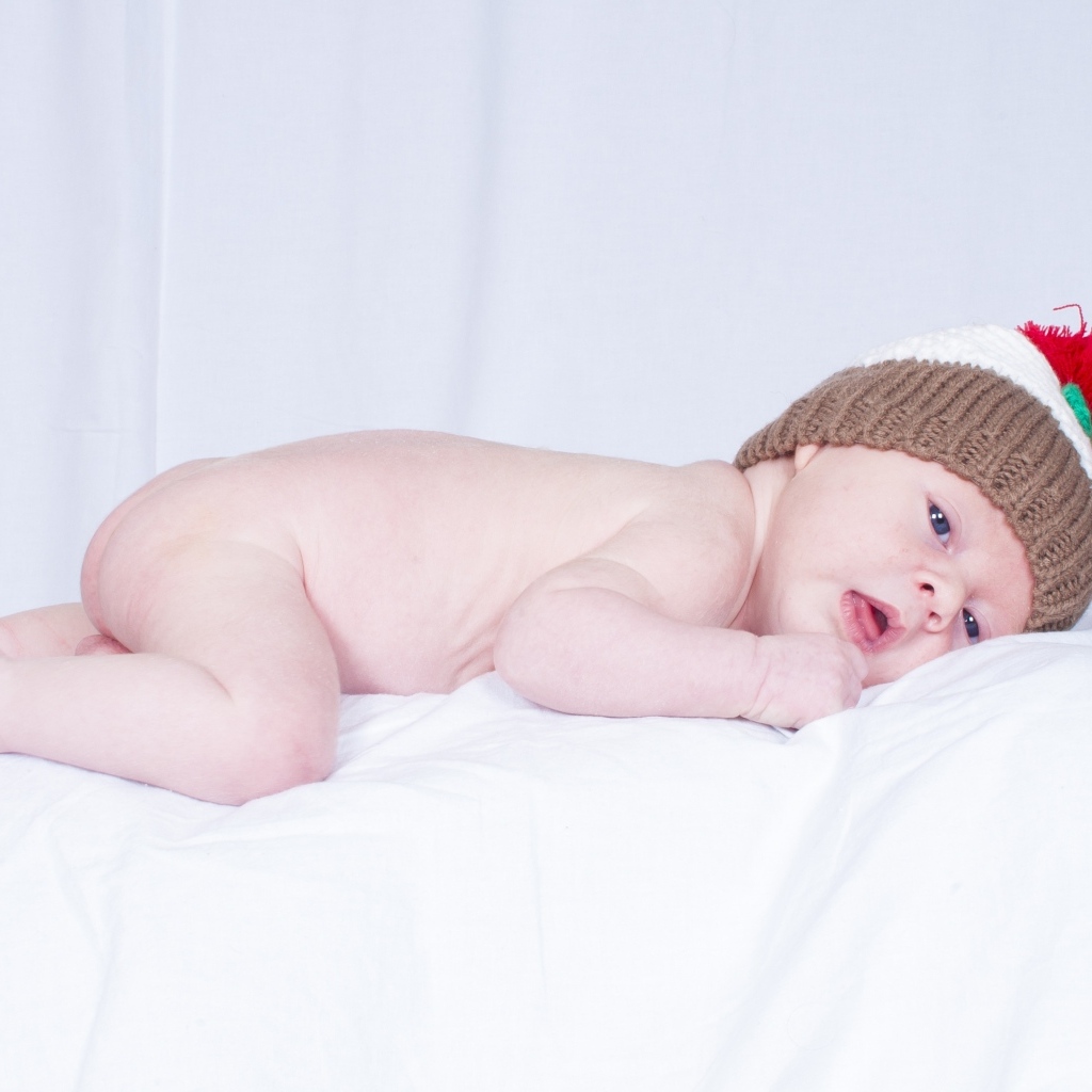 Новорожденный малыш в шапке на белой подушке