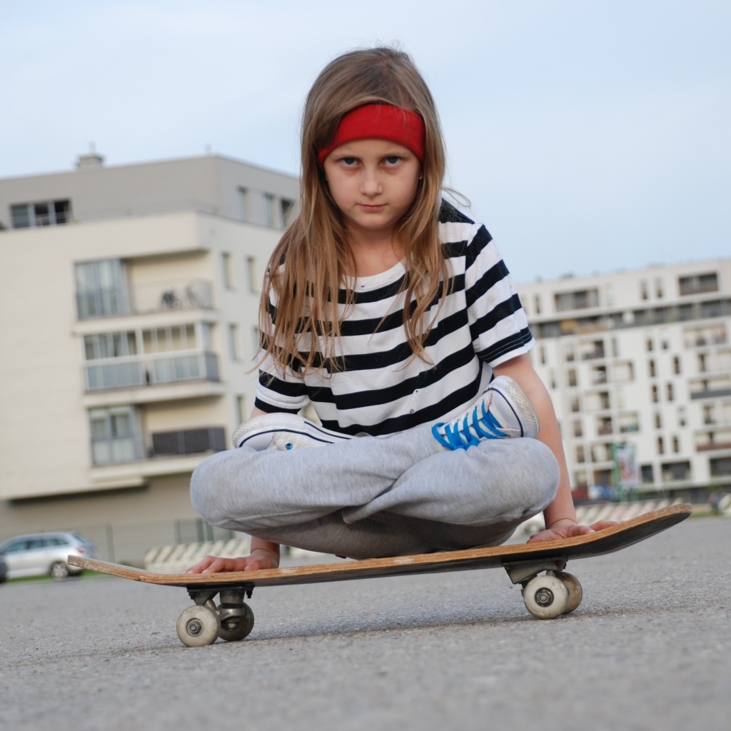 Серьезная девочка сидит на  скейтборде