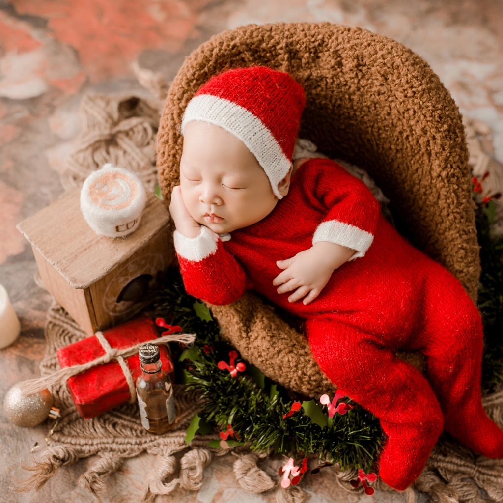 Спящий новорожденный ребенок в красном новогоднем костюме