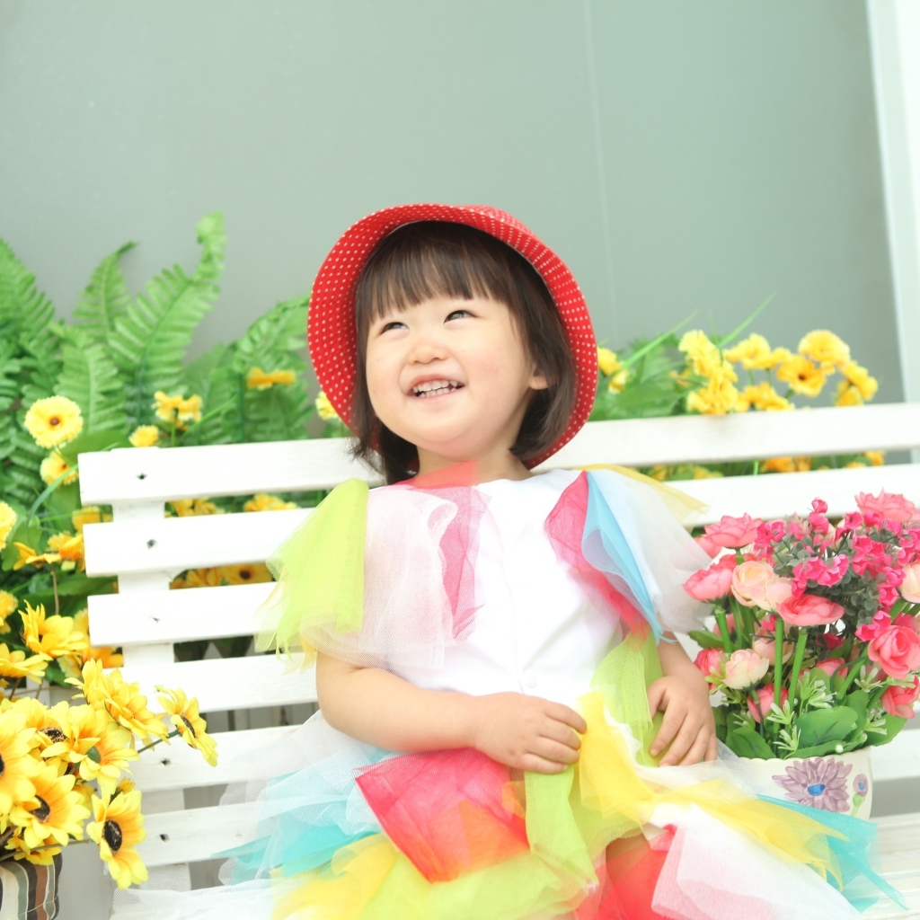 Улыбающаяся девочка азиатка сидит на лавке с цветами