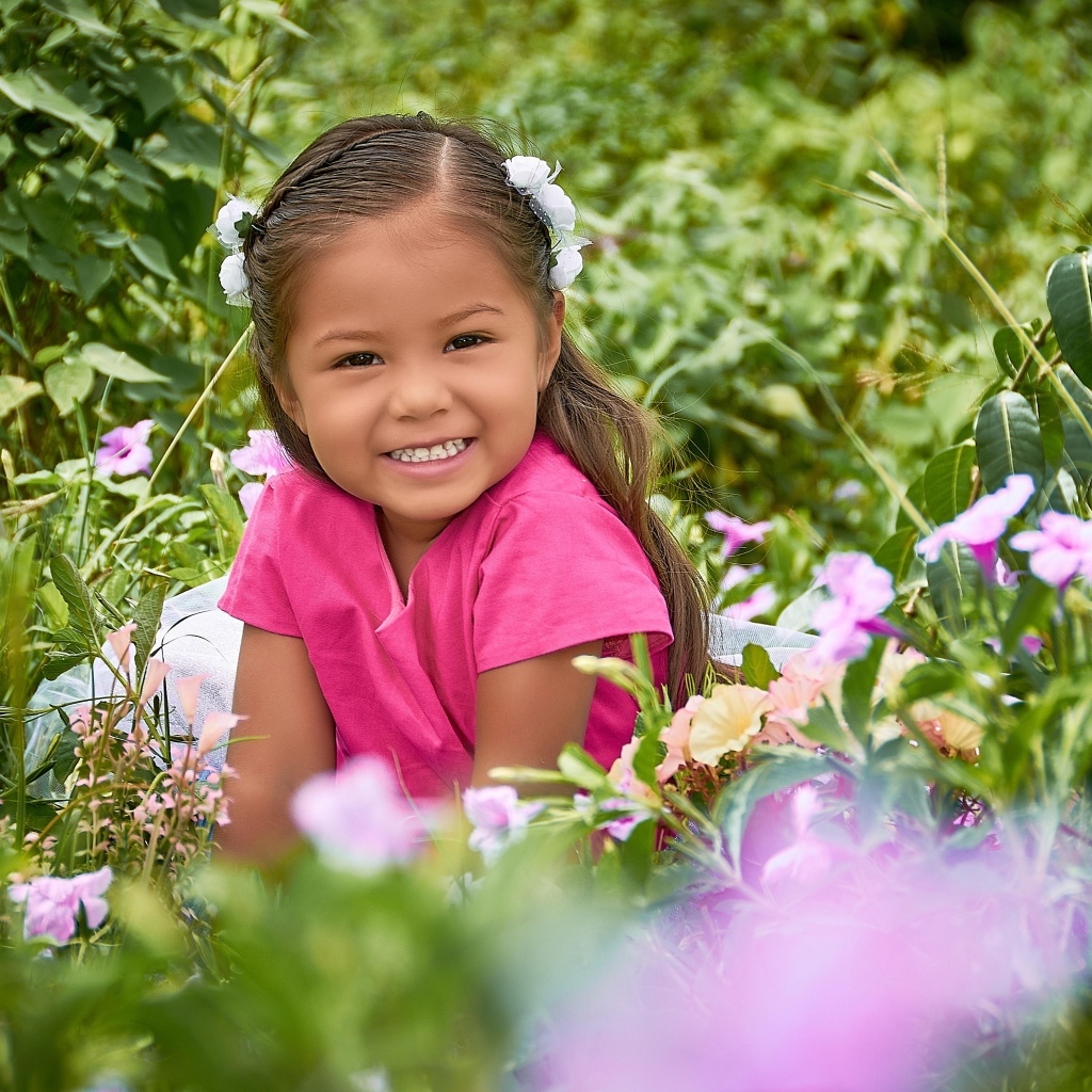 Улыбающаяся маленькая девочка сидит в цветах