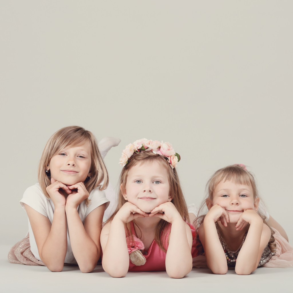 Три маленькие девочки лежат на сером фоне
