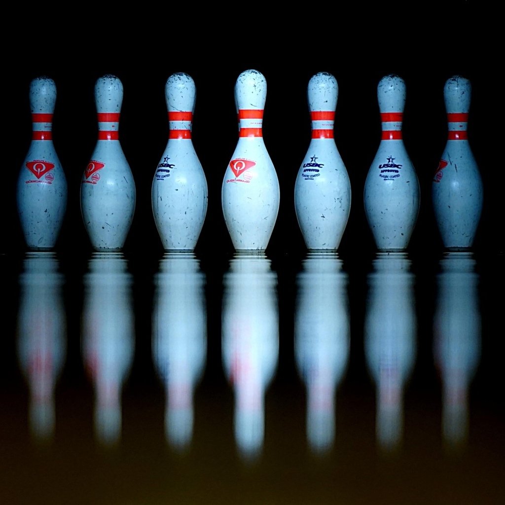 Кегли для боулинга отражаются в черной поверхности 