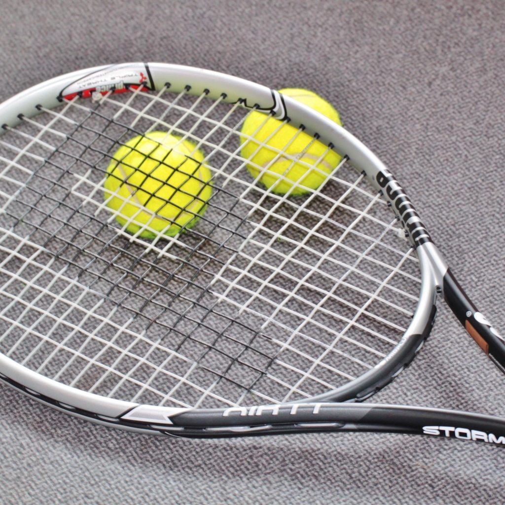 Ракетка и два мяча для тенниса на сером столе