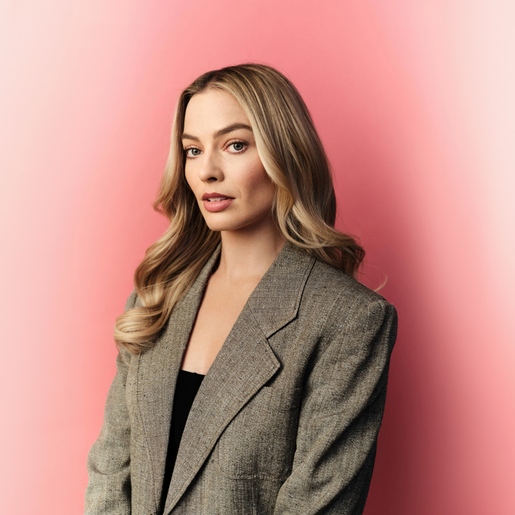 Актриса Марго Робби в сером пиджаке на розовом фоне