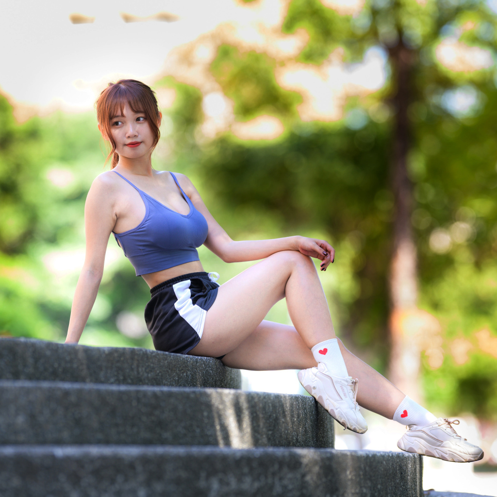 Спортивная азиатка в кроссовках сидит на ступеньках