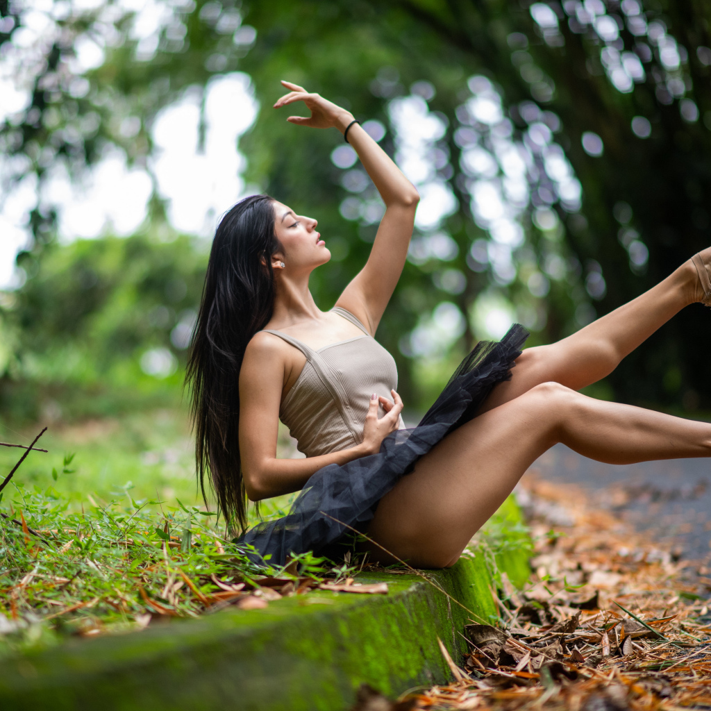 Девушка балерина в короткой юбке сидит на земле