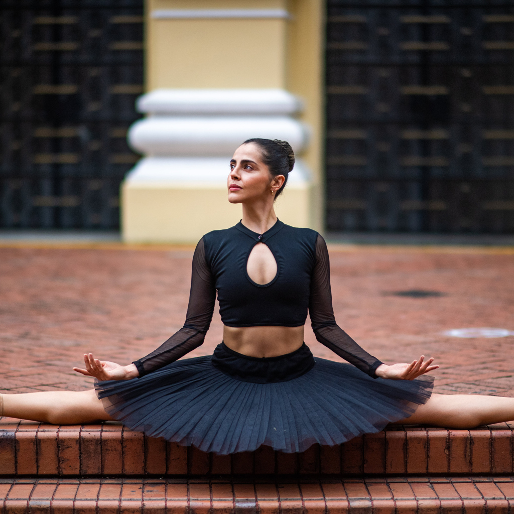 Девушка балерина в черном сидит на шпагате