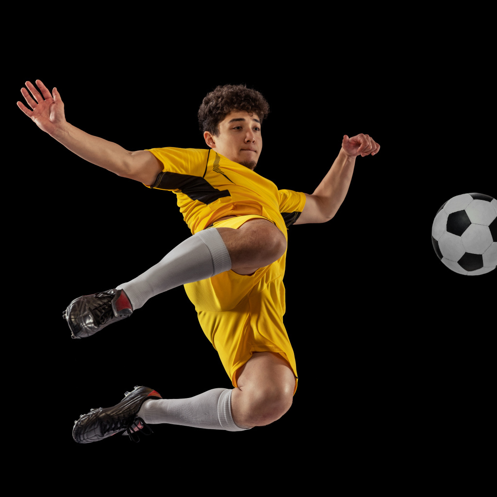 Мужчина футболист отбивает мяч на черном фоне