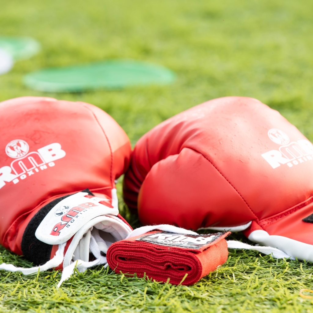 Красные боксерские перчатки лежат на зеленой траве 