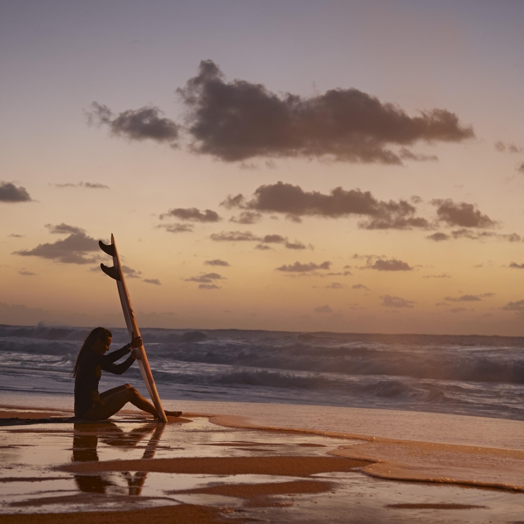 Девушка серфингистка сидит на берегу моря