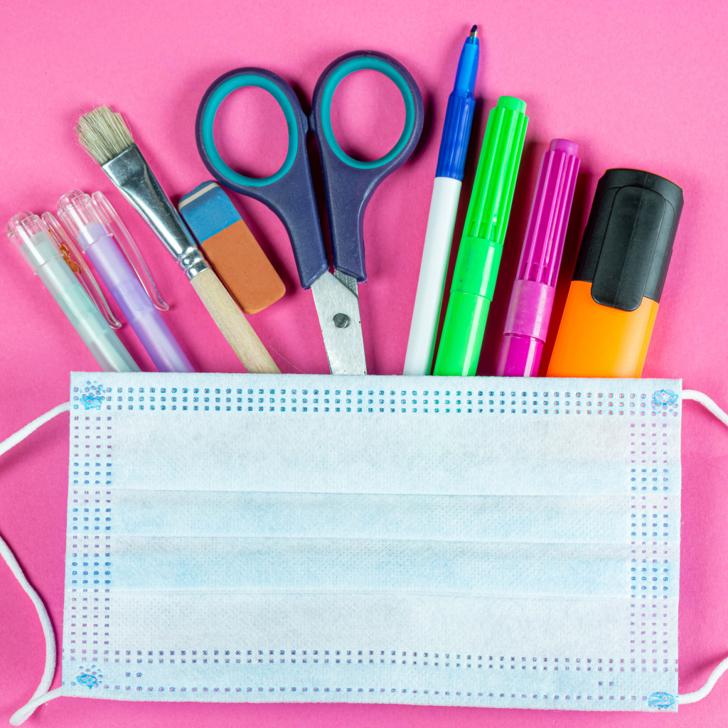 Канцелярские предметы и медицинская маска на розовом фоне