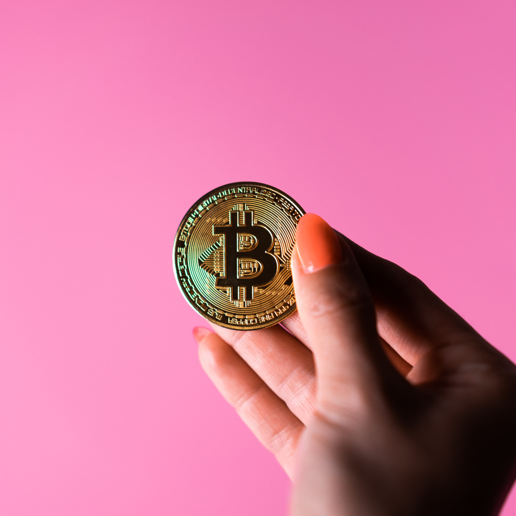 Золотая монета биткоин в руке девушки на розовом  фоне