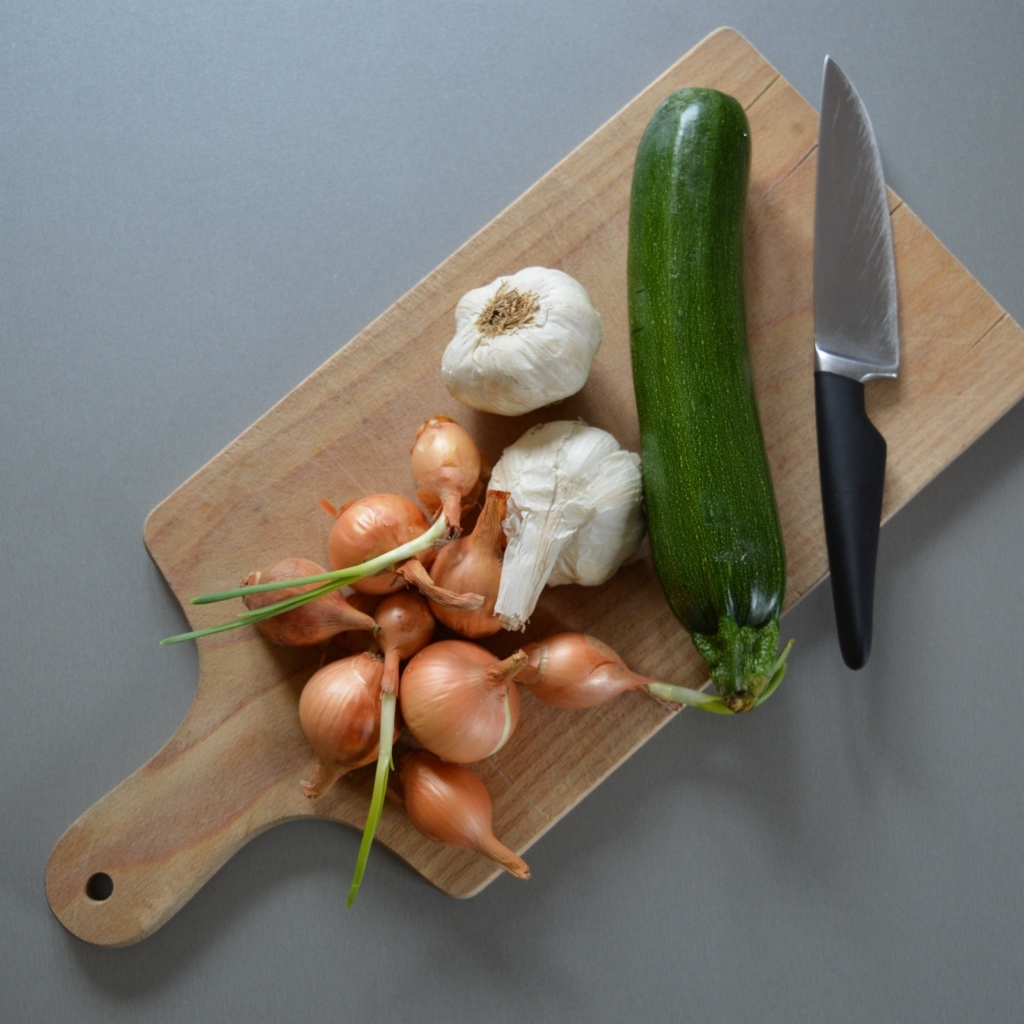 Лук, чеснок и кабачок на разделочной доске с ножом