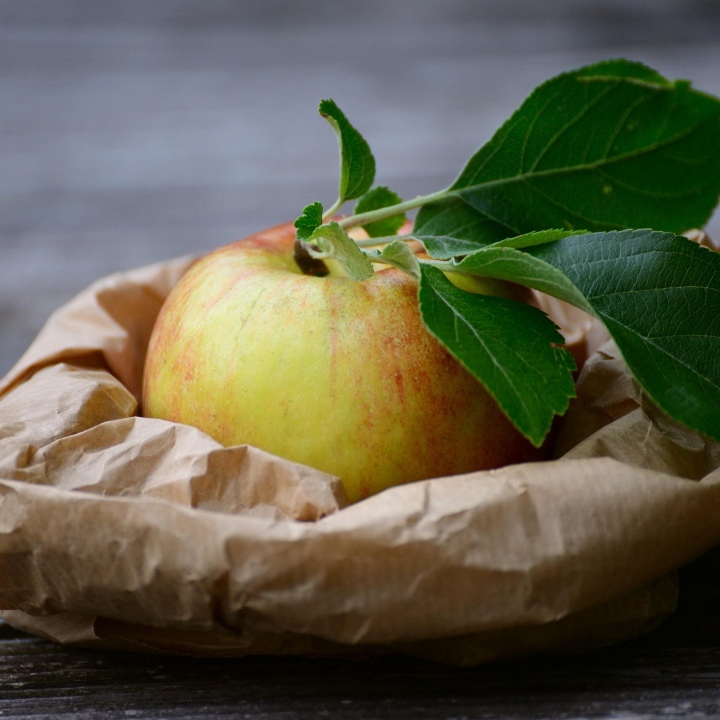 Яблоко с зелеными листьями на бумаге