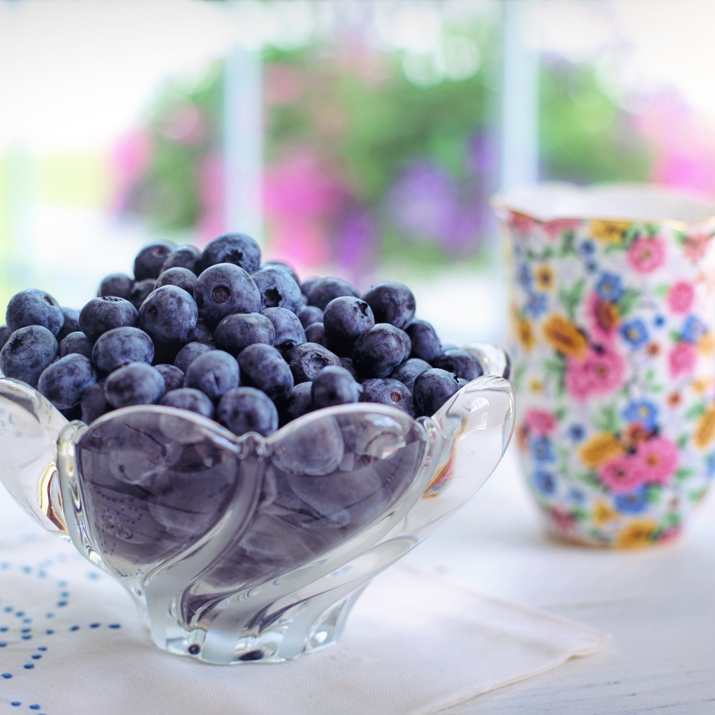 Черника в стеклянной вазе на столе с кружкой