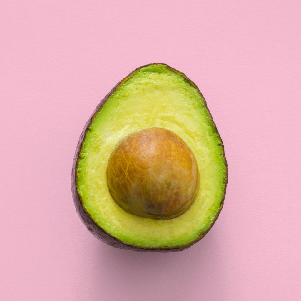 Половина авокадо с большой косточкой на розовом фоне