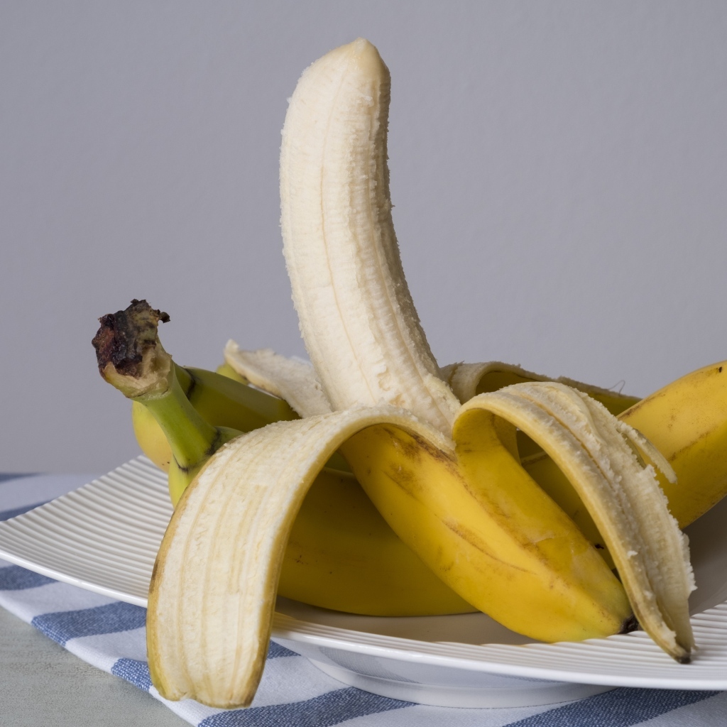 Очищенный банан на тарелке на сером фоне