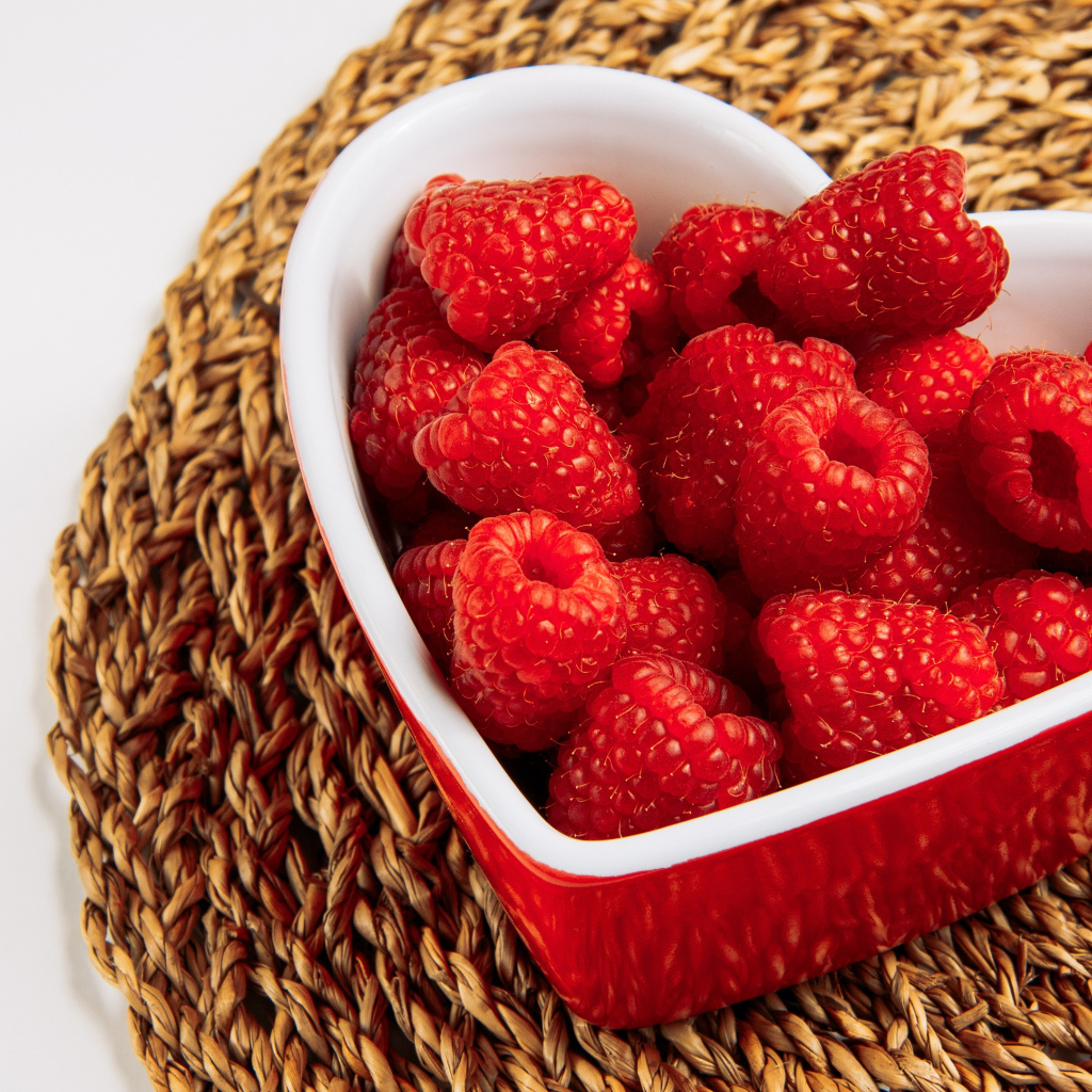 Малина в тарелке в виде сердца на столе