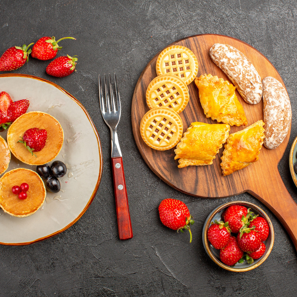 Печенье и оладьи на столе с ягодами клубники и виноградом