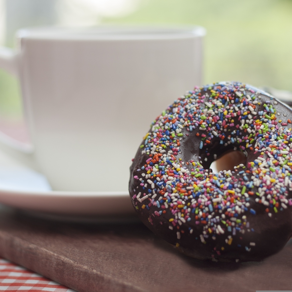 Донат с шоколадной глазурью и сладкой посыпкой на столе с чашкой чая