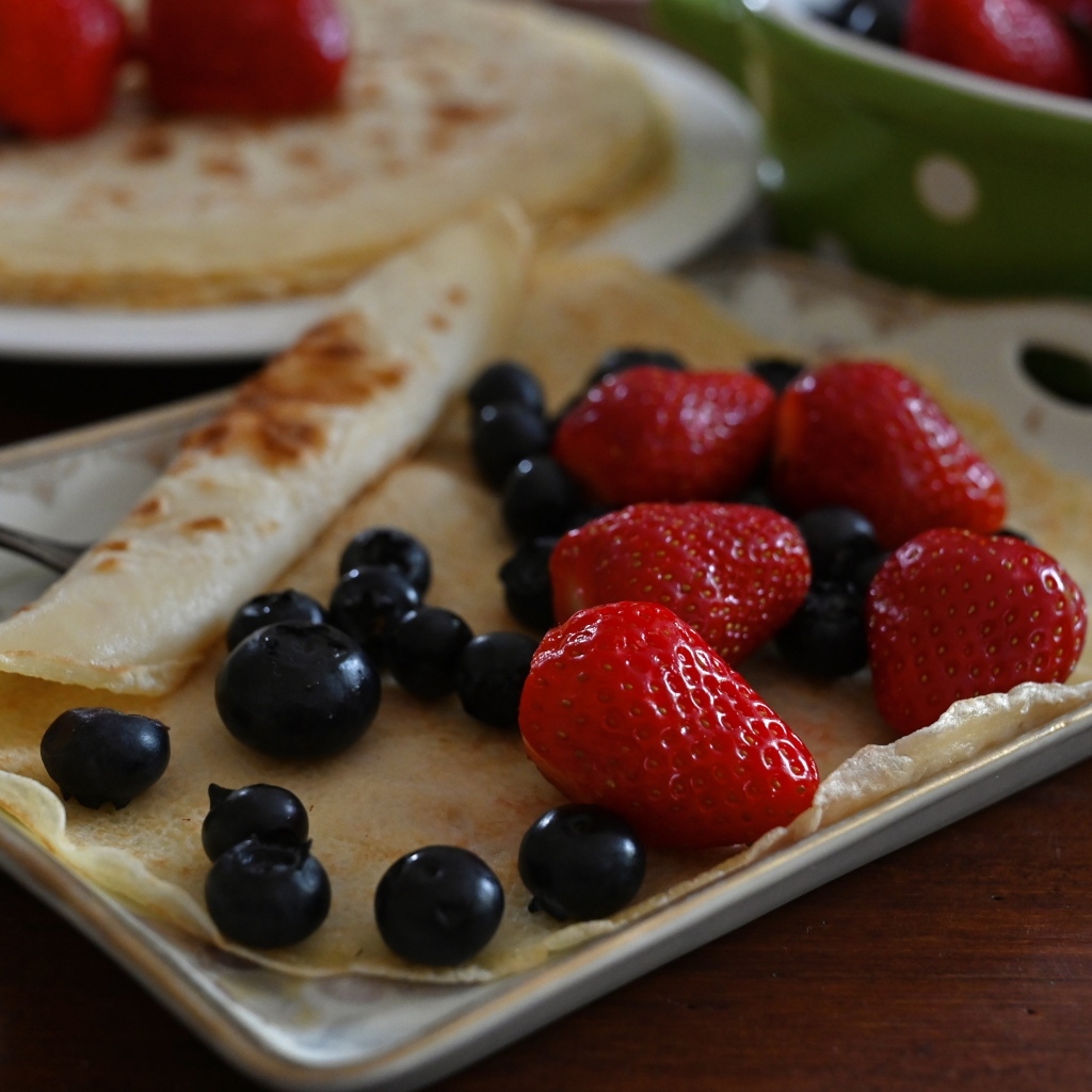 Блин с ягодами черники и клубники на тарелке