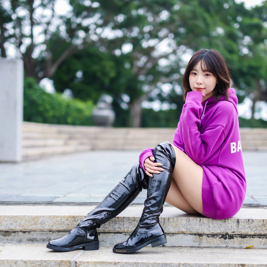 Девушка азиатка в длинных черных сапогах сидит на ступенях