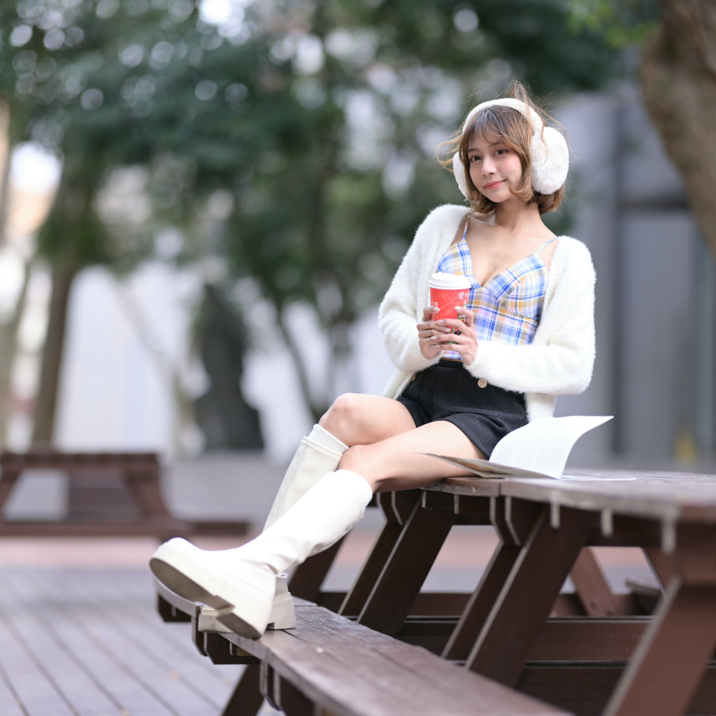 Девушка азиатка с кофе сидит на столе в парке