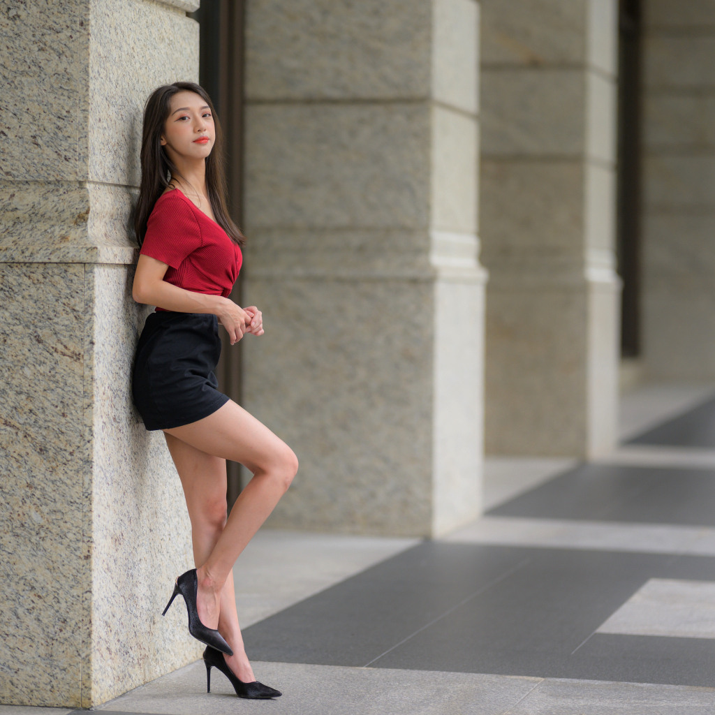 Азиатка в короткой черной юбке стоит у стены