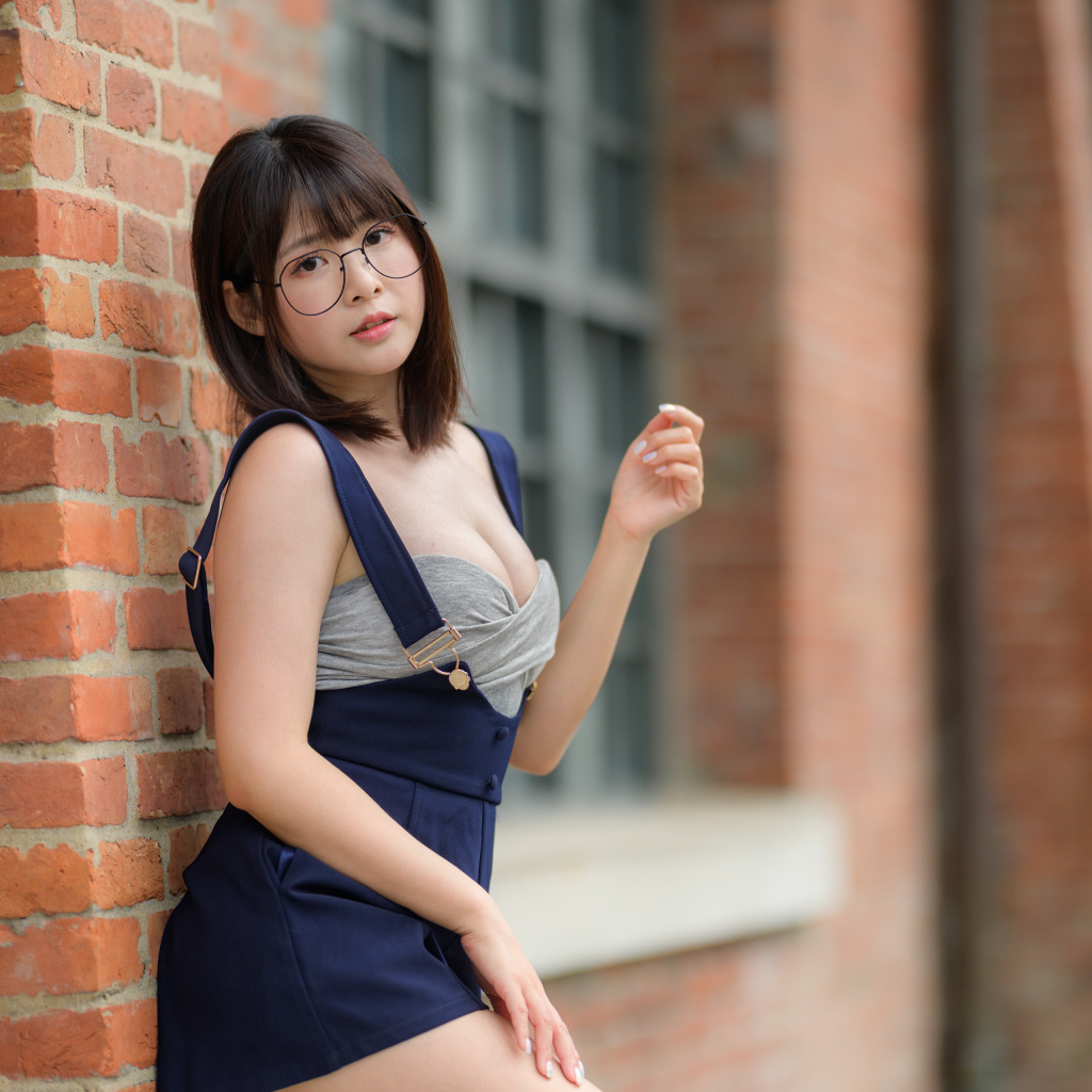 Азиатка в очках стоит у кирпичной стены