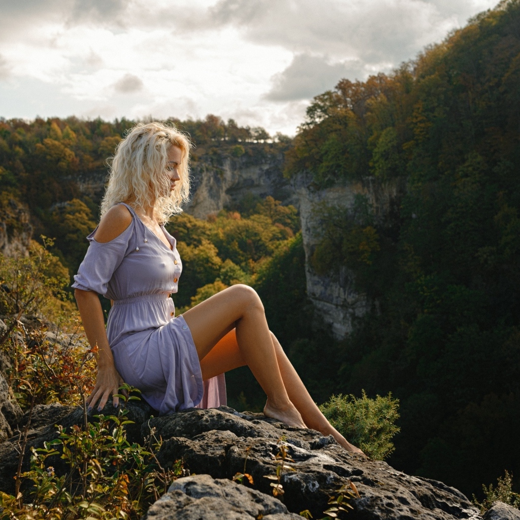Красивая длинноногая блондинка сидит на краю скалы